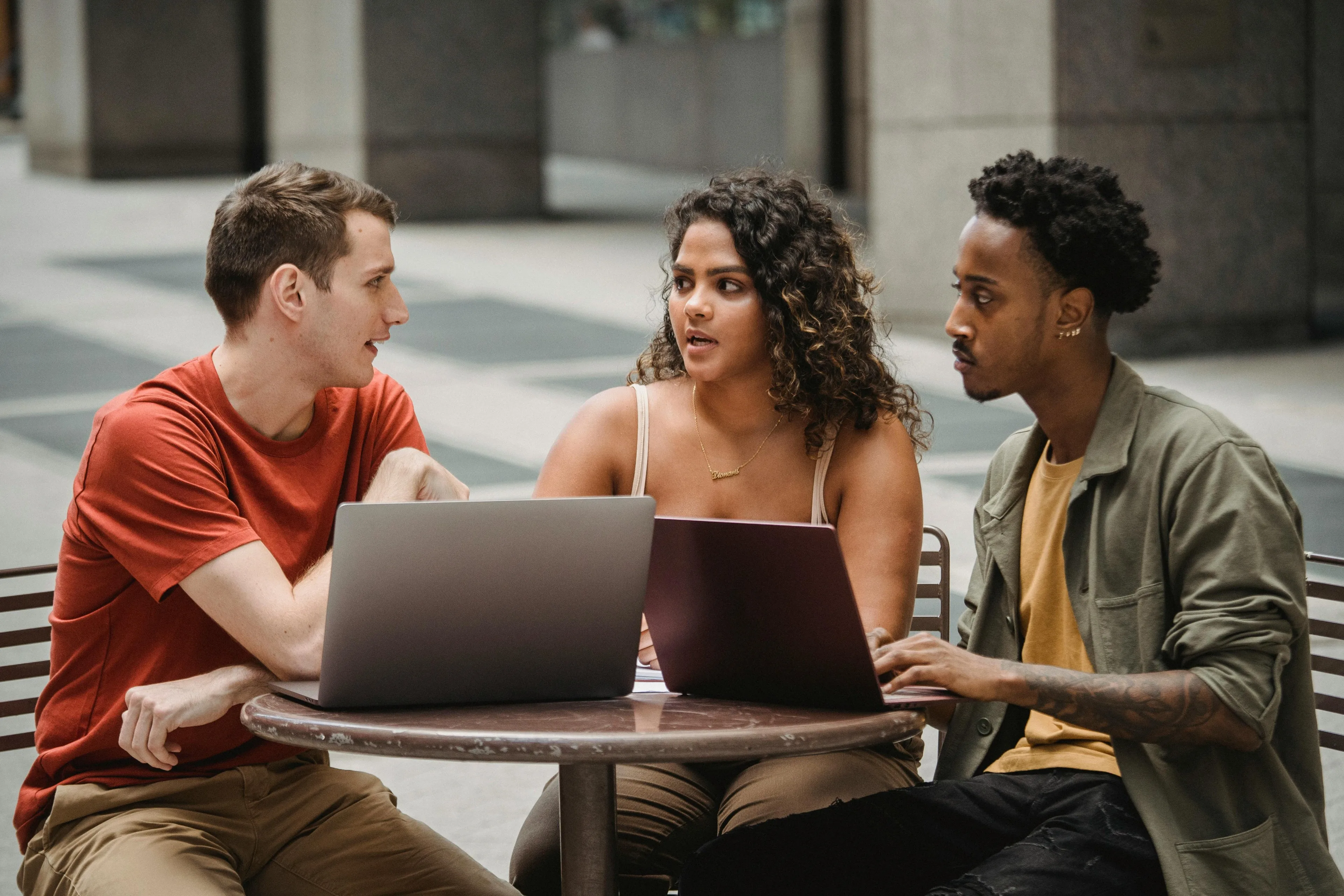 Three people discussing something outdoors behind a cafeteria table