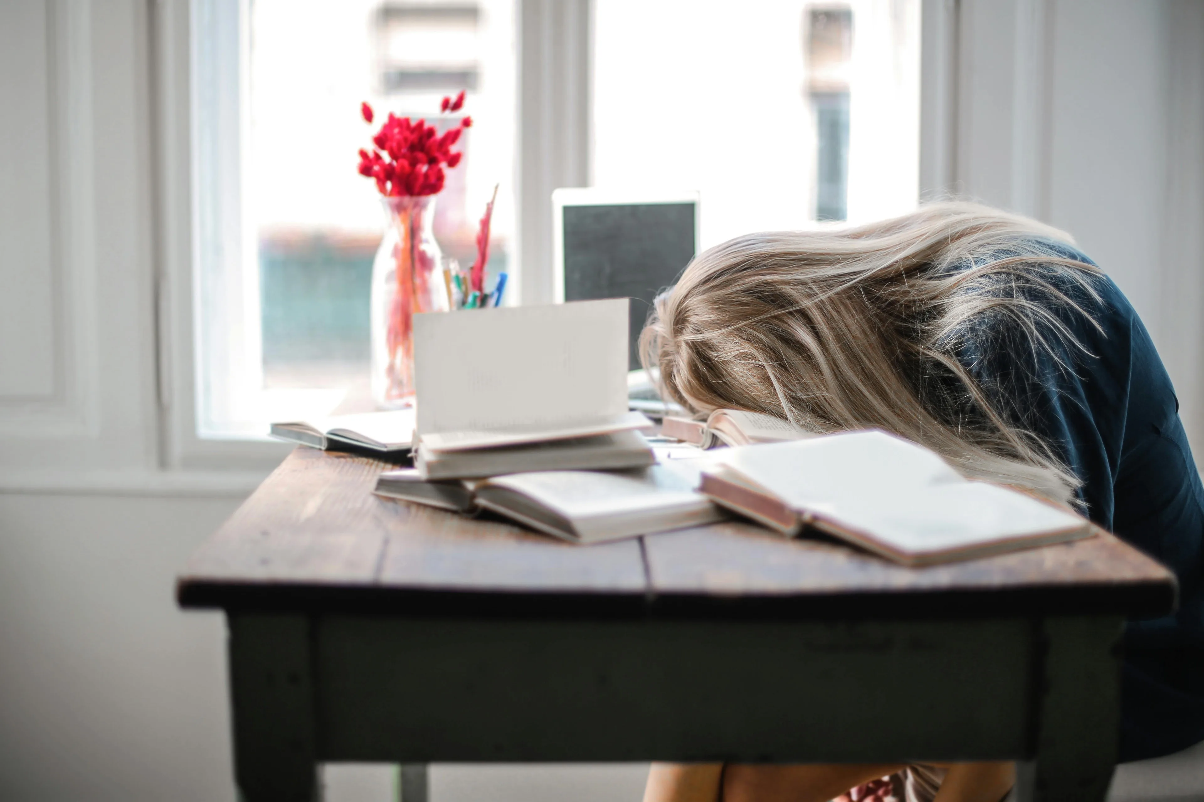 Exhausted woman resting her head on a desk covered with open books